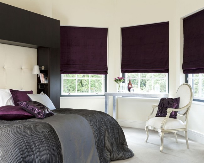 Purple roman blinds cardiff in a bedroom behind the bed and a dresser